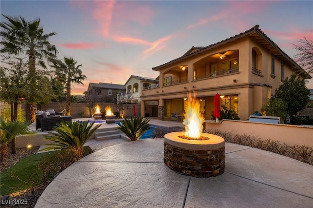 view of front of property featuring a patio, an outdoor living space with a fire pit, a balcony, and fence