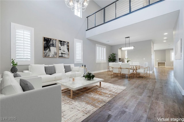 living room featuring wood finished floors, a towering ceiling, baseboards, and an inviting chandelier