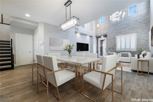 dining space featuring a towering ceiling, wood finished floors, stairs, a chandelier, and recessed lighting