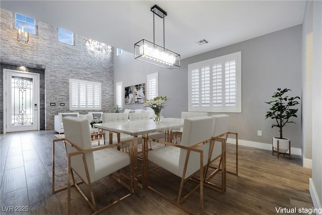 dining space featuring a notable chandelier, visible vents, a high ceiling, wood finished floors, and baseboards