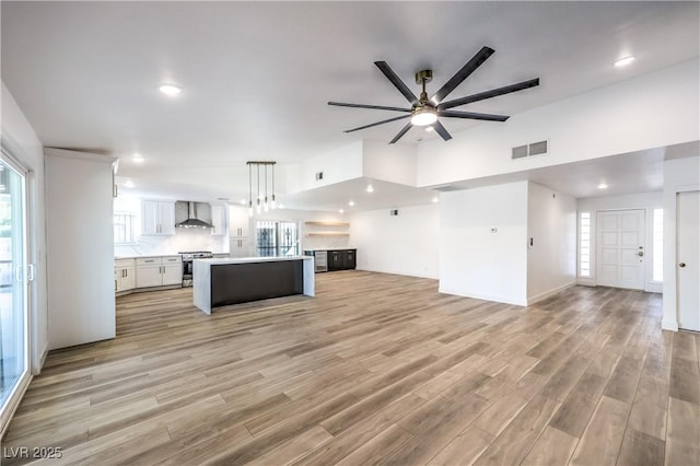 kitchen featuring white cabinets, stainless steel electric range oven, a kitchen island, open floor plan, and wall chimney range hood