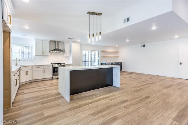 kitchen with hanging light fixtures, wall chimney range hood, stainless steel range, and light countertops