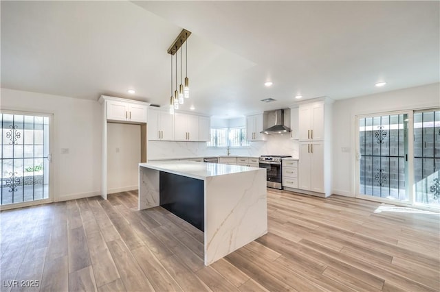 kitchen with stainless steel range with gas cooktop, a center island, hanging light fixtures, white cabinets, and wall chimney exhaust hood