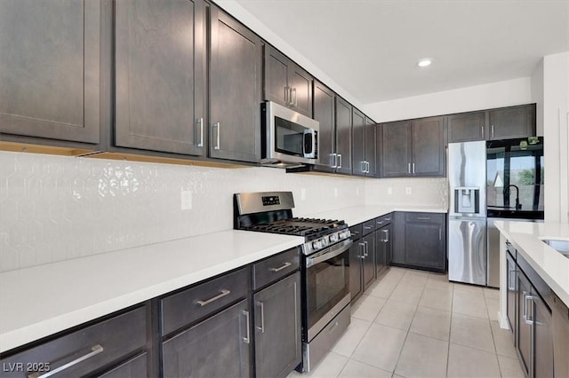 kitchen with light tile patterned floors, light countertops, appliances with stainless steel finishes, dark brown cabinets, and decorative backsplash