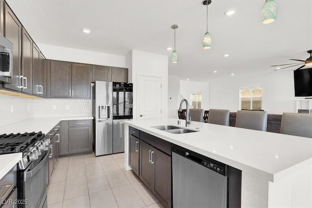 kitchen featuring a center island with sink, appliances with stainless steel finishes, hanging light fixtures, light countertops, and a sink