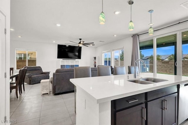 kitchen featuring a sink, a kitchen island with sink, light countertops, pendant lighting, and stainless steel dishwasher