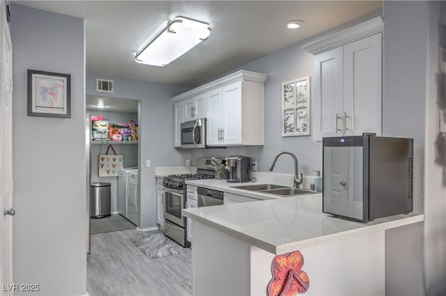 kitchen featuring visible vents, appliances with stainless steel finishes, white cabinets, a sink, and independent washer and dryer