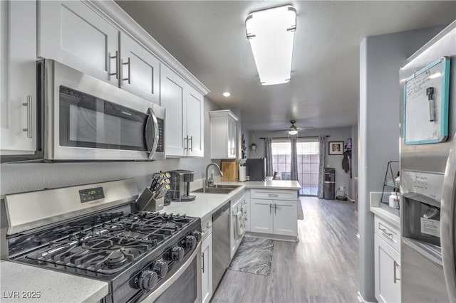 kitchen with stainless steel appliances, a peninsula, a sink, white cabinetry, and light countertops