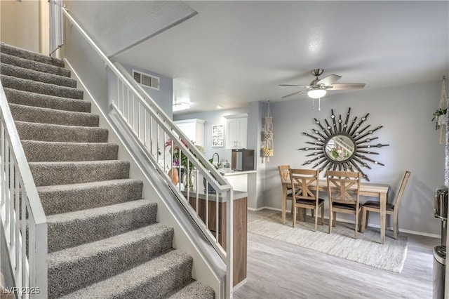 staircase with ceiling fan, wood finished floors, visible vents, and baseboards