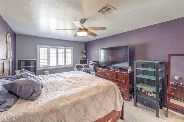 bedroom featuring light colored carpet, visible vents, a textured wall, a ceiling fan, and a textured ceiling