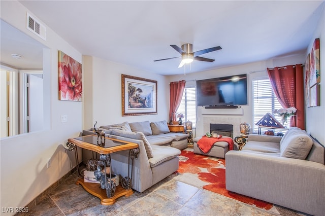 living area featuring ceiling fan, visible vents, baseboards, and a glass covered fireplace