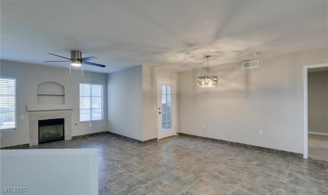 unfurnished living room with baseboards, a fireplace, visible vents, and ceiling fan