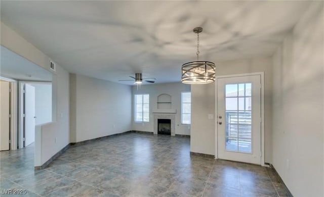 unfurnished living room with ceiling fan with notable chandelier, a fireplace, visible vents, and baseboards