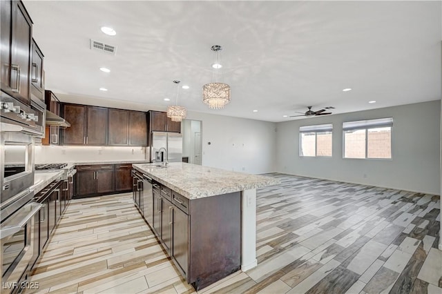 kitchen with visible vents, a center island with sink, a sink, dark brown cabinets, and ceiling fan