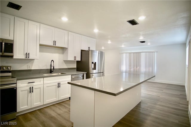 kitchen featuring stainless steel appliances, wood finished floors, a kitchen island, a sink, and visible vents