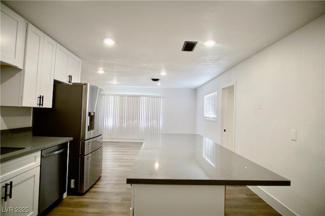 kitchen featuring light wood finished floors, stainless steel dishwasher, visible vents, and white cabinetry