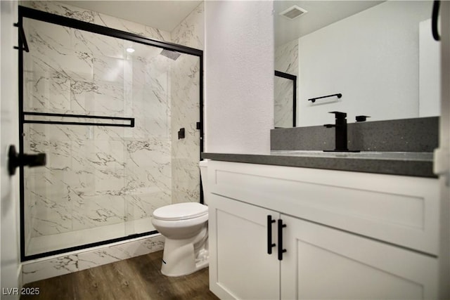 full bath with toilet, a marble finish shower, wood finished floors, and visible vents