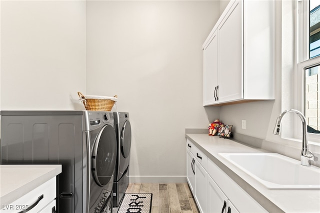 laundry room featuring cabinet space, baseboards, washer and dryer, light wood-type flooring, and a sink