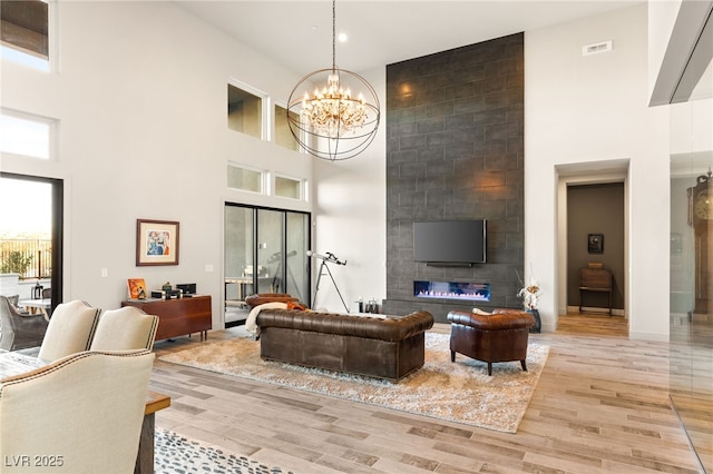 living area featuring light wood-style flooring, a large fireplace, a high ceiling, visible vents, and an inviting chandelier