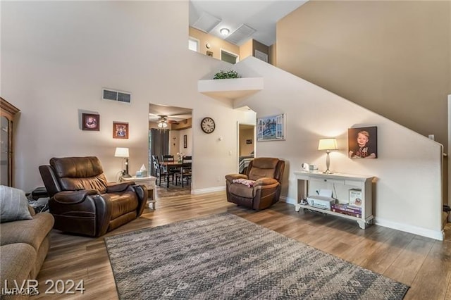 living room featuring baseboards, visible vents, a ceiling fan, wood finished floors, and a high ceiling