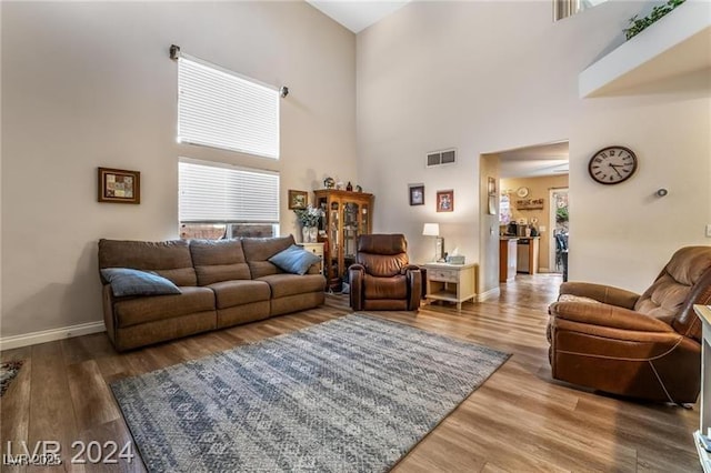 living room featuring a towering ceiling, wood finished floors, visible vents, and baseboards