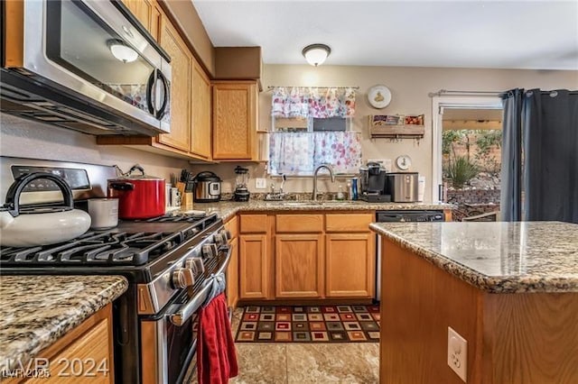 kitchen with appliances with stainless steel finishes, brown cabinetry, a sink, and light stone countertops