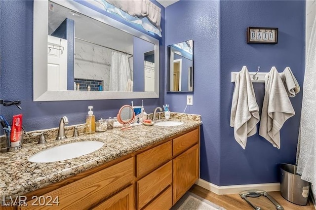 bathroom with wood finished floors, a sink, baseboards, and double vanity