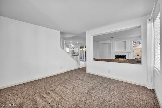 unfurnished living room featuring stairway, carpet flooring, a lit fireplace, and baseboards