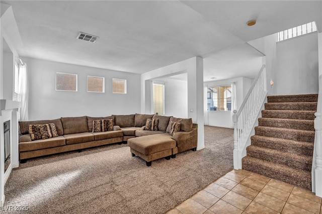 living room with light tile patterned floors, light colored carpet, visible vents, stairway, and a glass covered fireplace