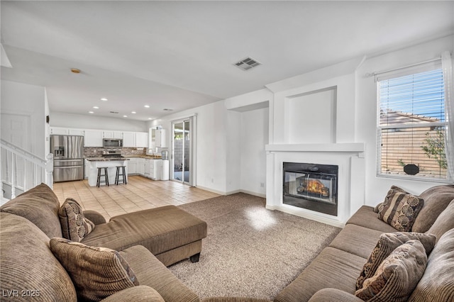 living room featuring light tile patterned floors, plenty of natural light, visible vents, and a glass covered fireplace