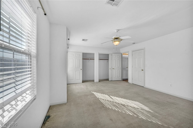 unfurnished bedroom with baseboards, carpet, visible vents, and two closets