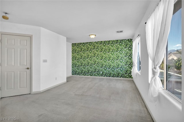 carpeted empty room with an accent wall, visible vents, and baseboards