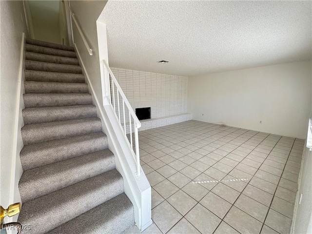 staircase with a textured ceiling, a brick fireplace, and tile patterned floors