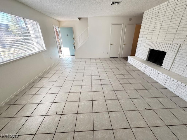 unfurnished living room with visible vents, stairway, a textured ceiling, a fireplace, and light tile patterned flooring