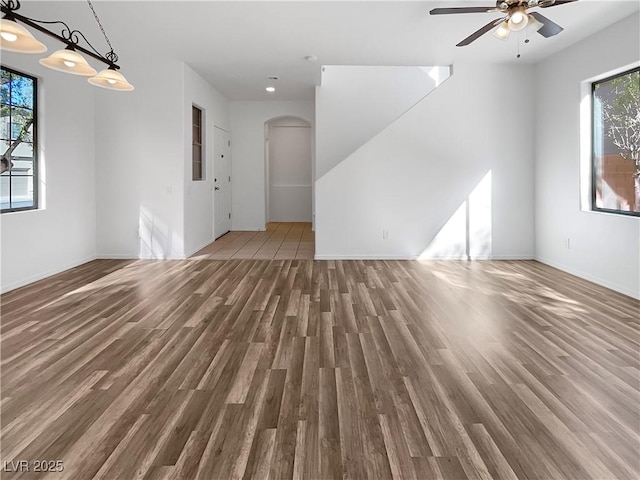 unfurnished living room featuring ceiling fan, arched walkways, and wood finished floors