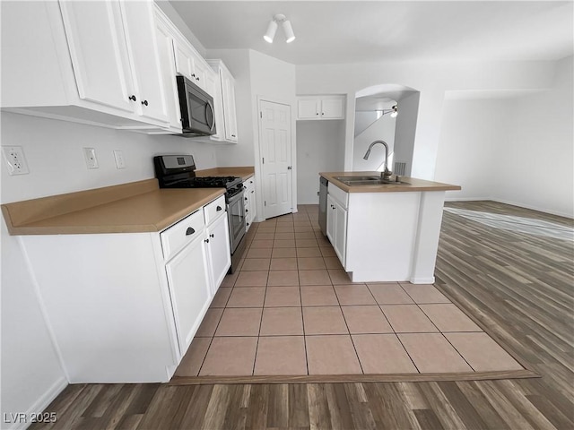 kitchen featuring a kitchen island with sink, a sink, white cabinets, appliances with stainless steel finishes, and light wood finished floors