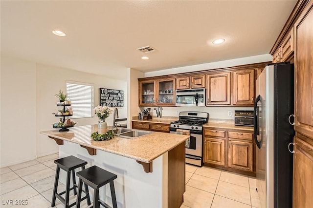 kitchen with appliances with stainless steel finishes, brown cabinetry, a sink, and light tile patterned floors