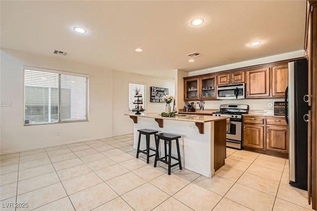 kitchen with light tile patterned floors, stainless steel appliances, visible vents, and a kitchen breakfast bar