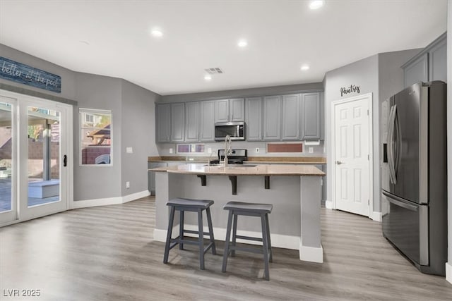 kitchen with recessed lighting, light wood-style flooring, gray cabinetry, appliances with stainless steel finishes, and a kitchen island with sink