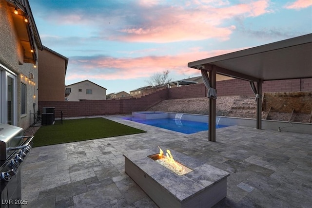 pool at dusk featuring a patio, an outdoor fire pit, a fenced backyard, and a fenced in pool