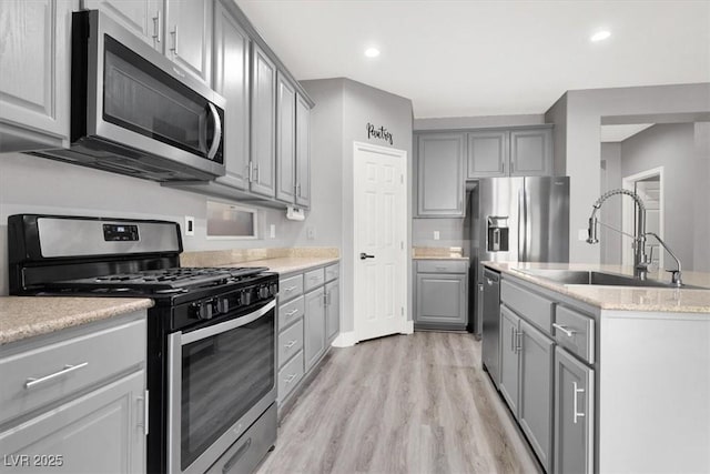 kitchen featuring stainless steel appliances, recessed lighting, gray cabinetry, light wood-style floors, and a sink