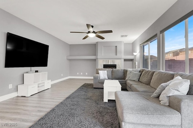 living room with visible vents, ceiling fan, wood finished floors, a tile fireplace, and baseboards