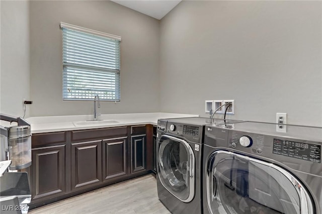 clothes washing area featuring light wood finished floors, cabinet space, separate washer and dryer, and a sink