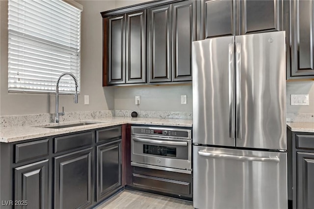 kitchen featuring appliances with stainless steel finishes, a sink, and light stone countertops