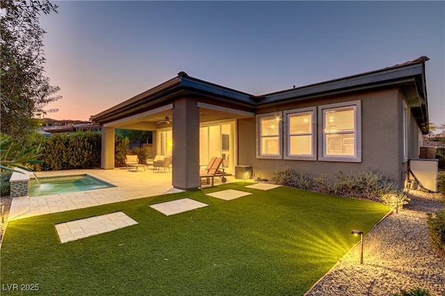 back of property at dusk with ceiling fan, a patio, a yard, and stucco siding