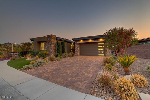 view of front facade with stone siding, decorative driveway, an attached garage, and stucco siding