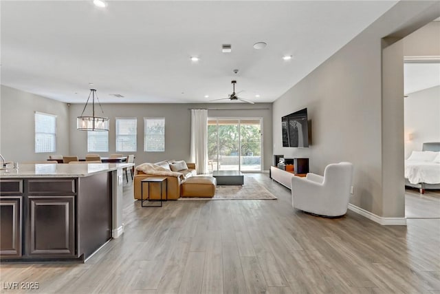 living room featuring baseboards, light wood finished floors, a chandelier, and recessed lighting