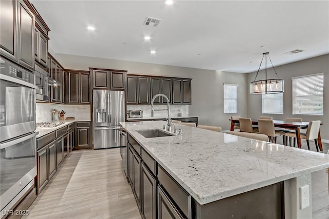 kitchen featuring a sink, visible vents, appliances with stainless steel finishes, backsplash, and a large island with sink