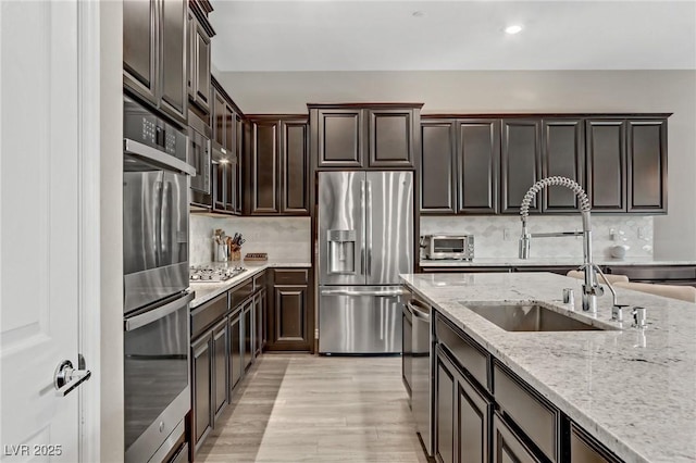 kitchen with light stone counters, stainless steel appliances, backsplash, a sink, and light wood-type flooring