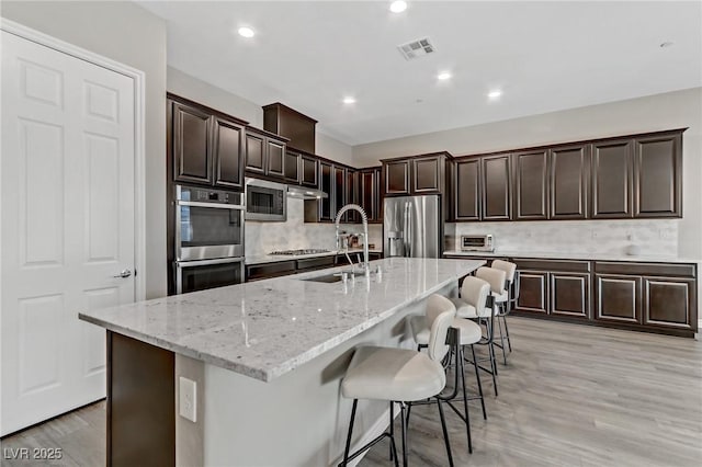 kitchen featuring light stone counters, stainless steel appliances, visible vents, a sink, and a kitchen breakfast bar